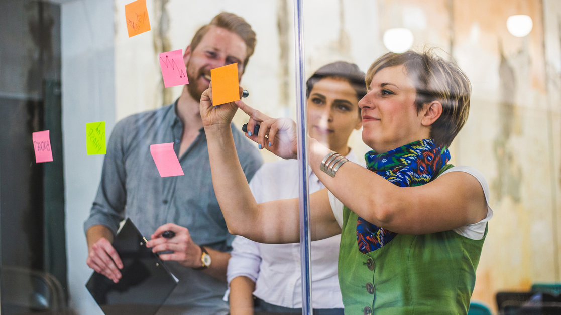 Three business professionals sticking post-it notes to an office wall while working together