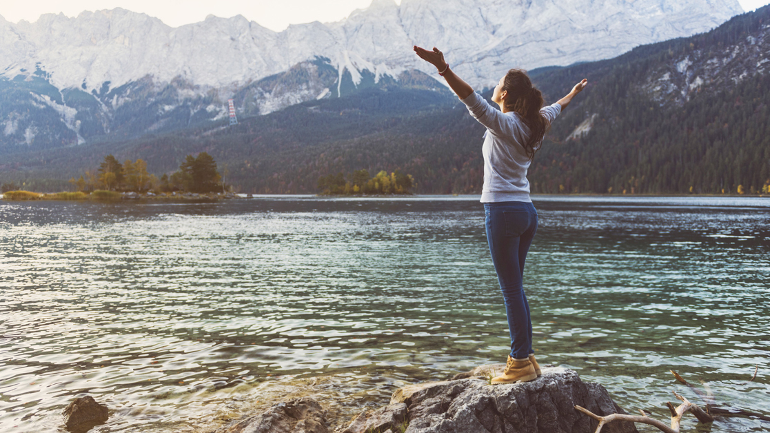 Woman standing on a rock overlooking the water with mountains in the background