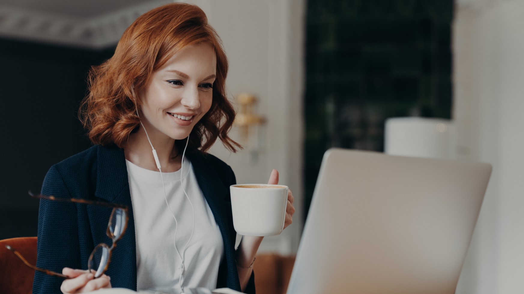 women sat at laptop smiling drinks aromatic coffee holding glasses in hand and dressed formally