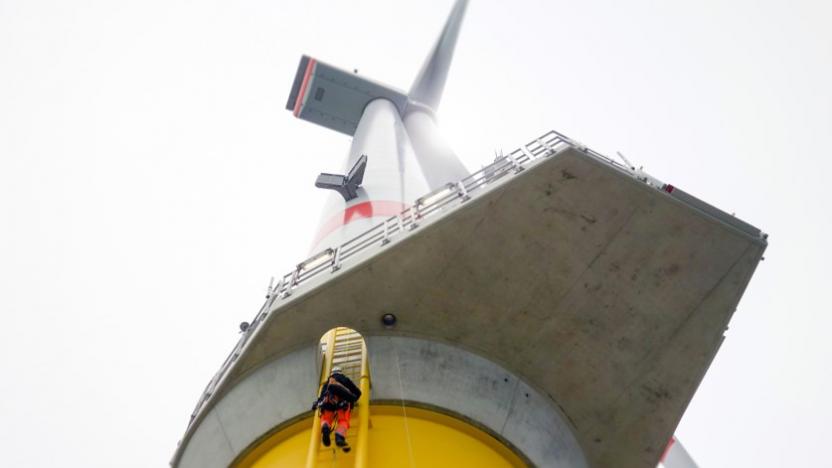 Manual high worker offshore climbing on wind-turbine on ladder in north sea